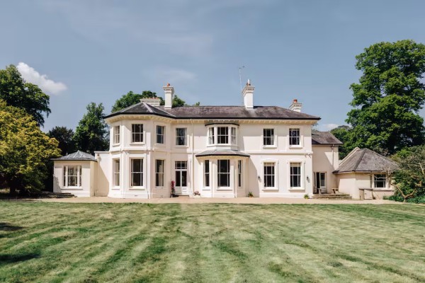 Elegant white Georgian-style country house with manicured lawn and classic sash windows under a blue sky