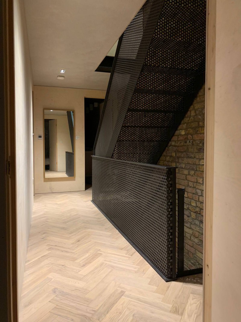 Contemporary hallway with herringbone wooden flooring, exposed brick wall, and perforated metal staircase