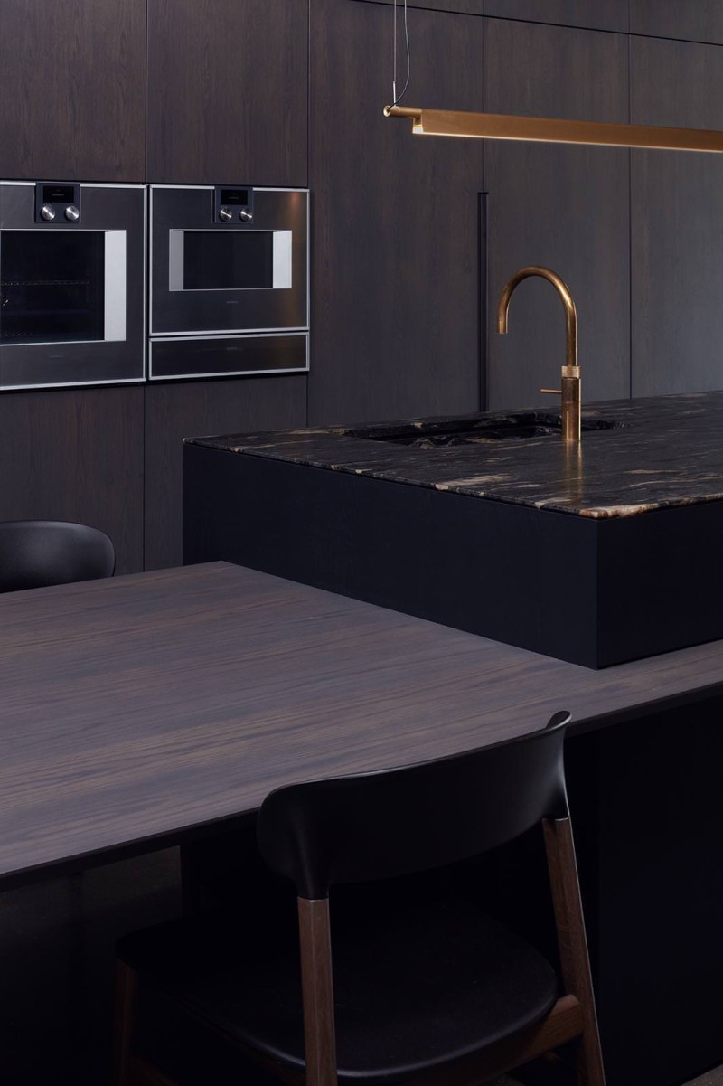 Dark modern kitchen with marble island, gold tap, integrated appliances, and steel-framed glass partition