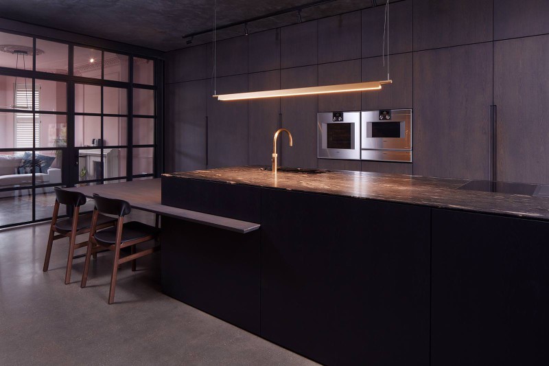 Dark modern kitchen with marble island, gold tap, integrated appliances, and steel-framed glass partition