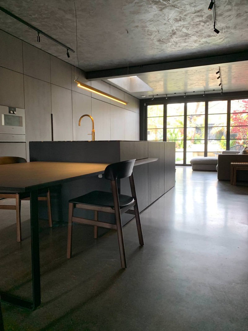 Minimalist kitchen with matte cabinetry, gold tap, and open-plan layout leading to garden views