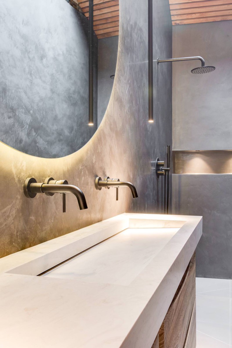 Close-up of minimalist bathroom vanity with integrated sink, black wall-mounted taps, and soft backlit mirror