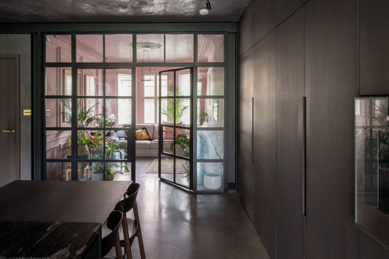 Steel-framed glass doors leading to pink-toned lounge with bay window and lush indoor plants