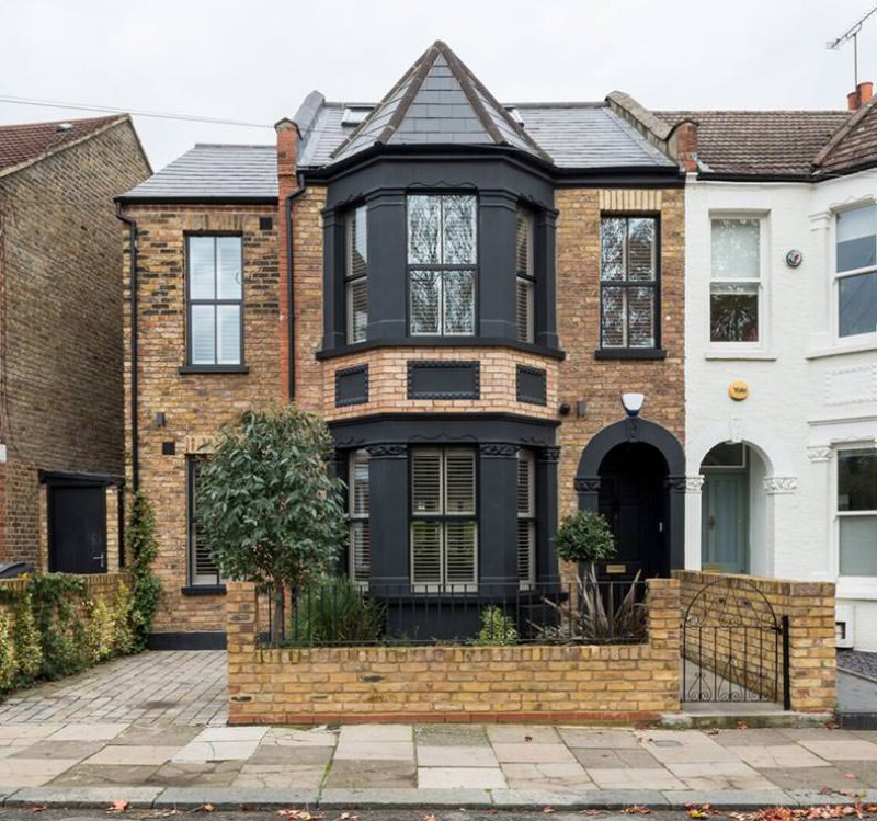 Renovated Victorian terraced house with modern black-framed bay windows and brick façade in London