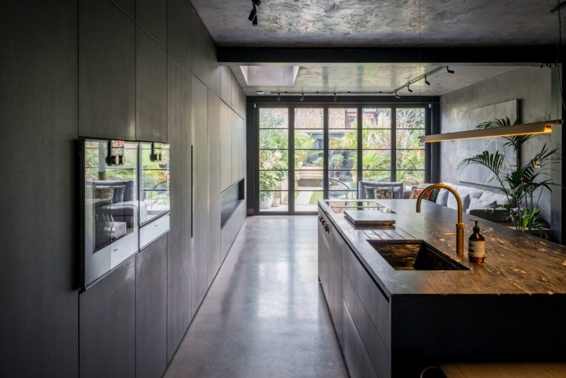 Sleek modern kitchen with dark island, gold tap, and full-height glass doors opening to tropical garden