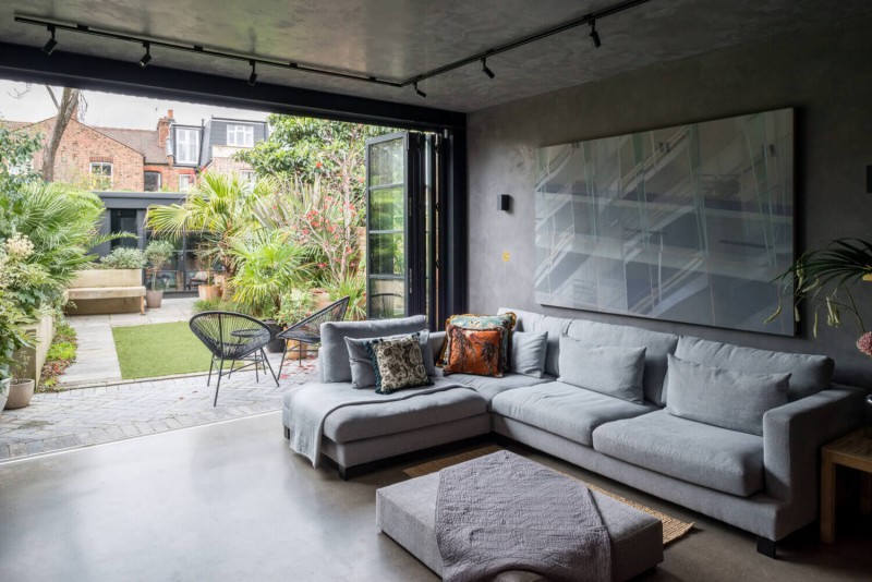 Modern living room with grey sectional sofa and folding glass doors opening to lush landscaped garden