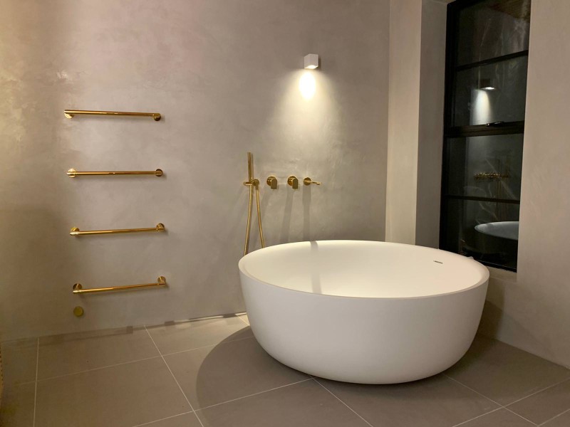 Elegant bathroom with round freestanding tub, gold fixtures, and microcement walls for a spa-like feel
