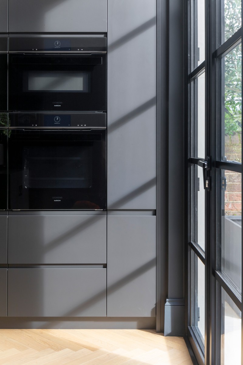Built-in Siemens appliances within matte grey kitchen cabinetry beside black-framed patio doors