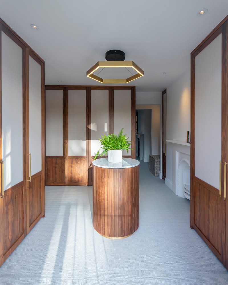 Elegant walk-in wardrobe with wood-panelled doors, central island with marble top, and gold hexagon ceiling light