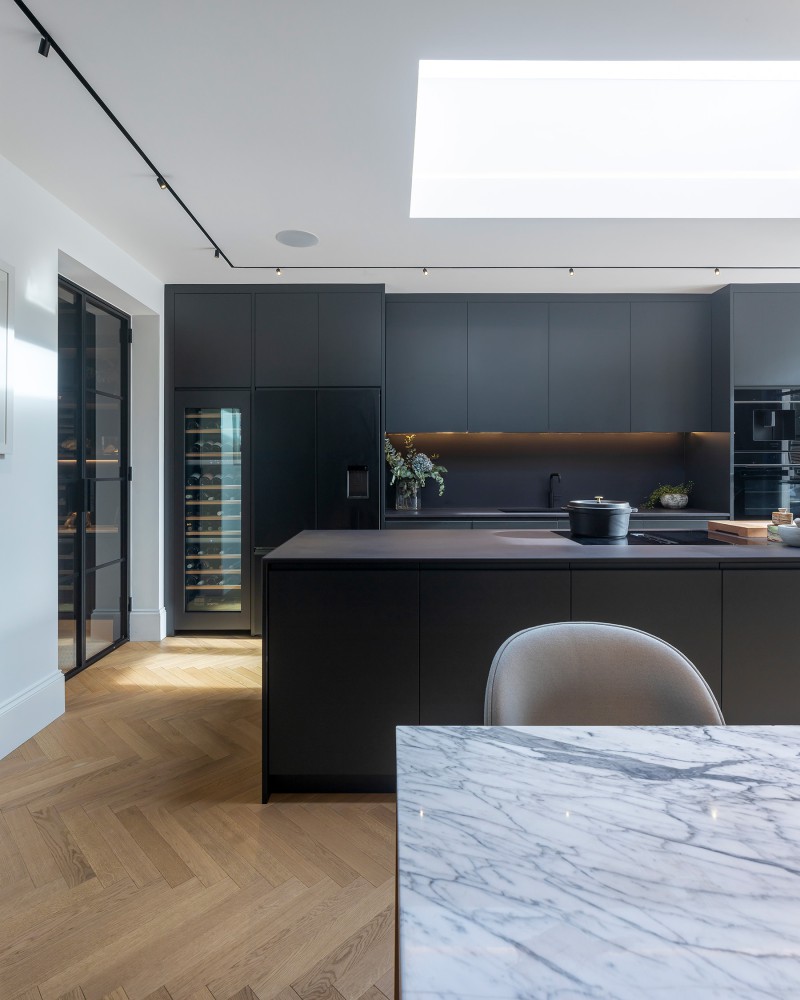 Luxury contemporary kitchen with matte black cabinetry, marble dining table, herringbone flooring, and skylight