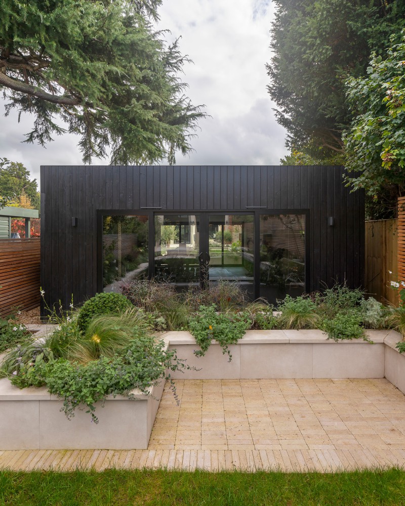 Contemporary black timber garden room with large glazed doors, surrounded by raised planters and mature trees
