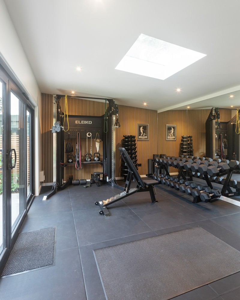 Modern home gym with Eleiko equipment, free weights, wooden slat wall panelling, and skylight above rubber flooring