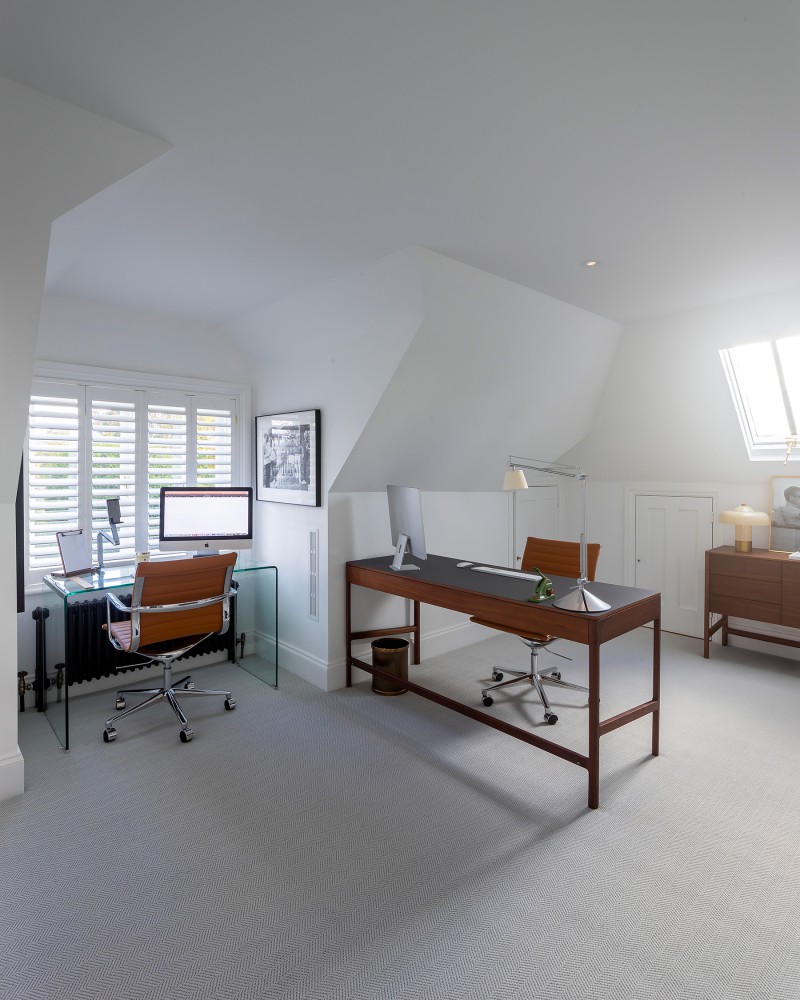 Bright and modern home office with dual workstations, mid-century chairs, skylight, and white shuttered windows