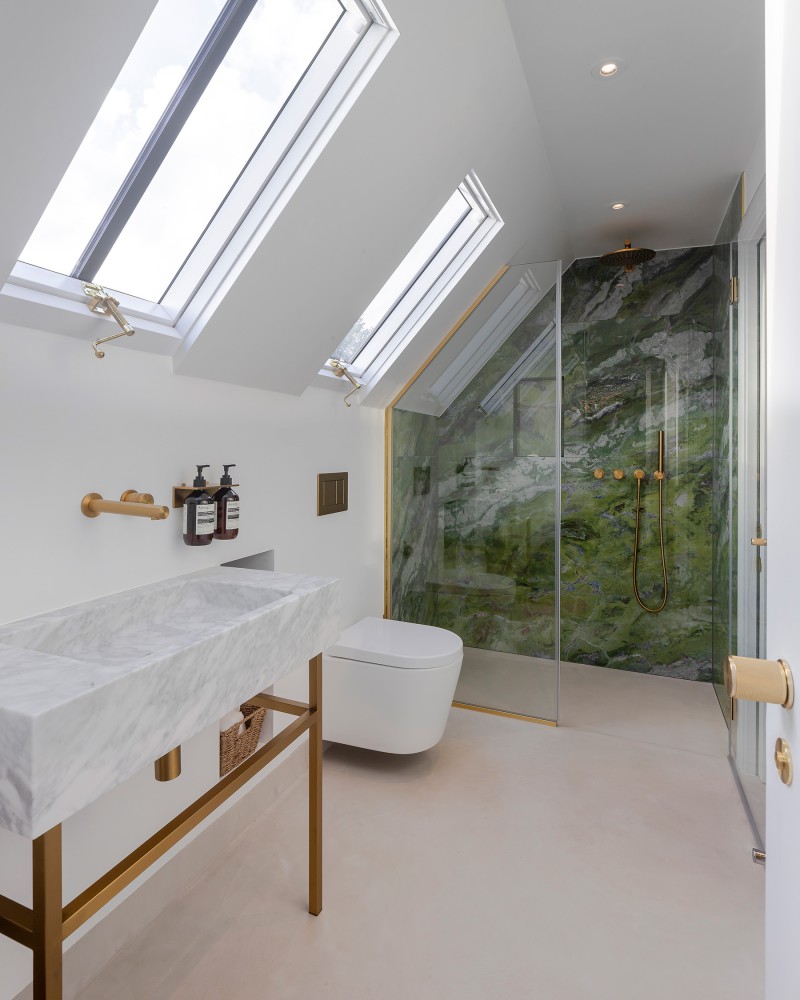 Contemporary bedroom with white walls, mirrored wardrobe, green accent cushions, and an ensuite bathroom with skylight and glass shower enclosure