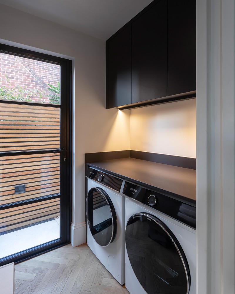 Contemporary utility room with integrated Siemens washer and dryer, black cabinetry, and under-cabinet lighting next to a glazed door