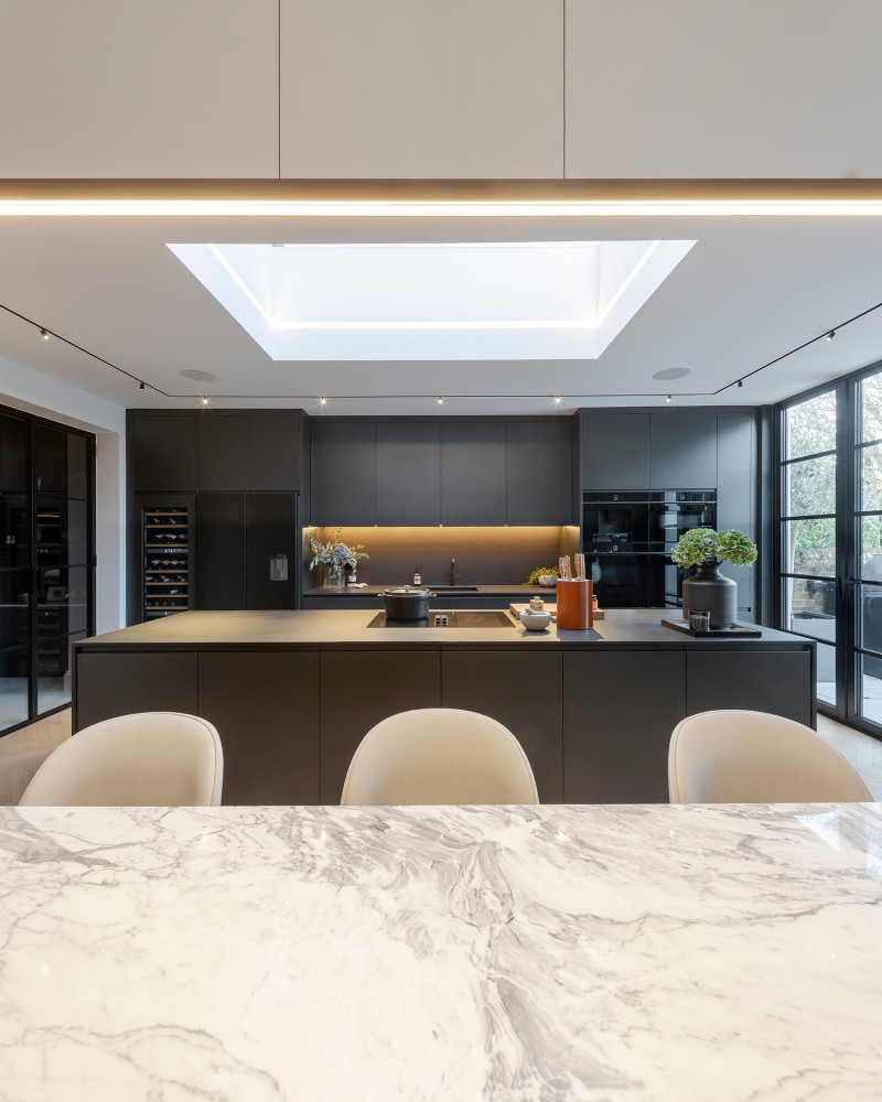 Luxury kitchen with marble dining table, black cabinetry, central island and skylight feature above