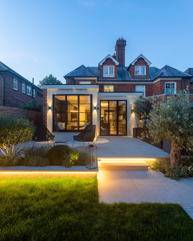 Rear elevation of Edwardian home with modern extension, illuminated garden steps, and black steel-framed glazing