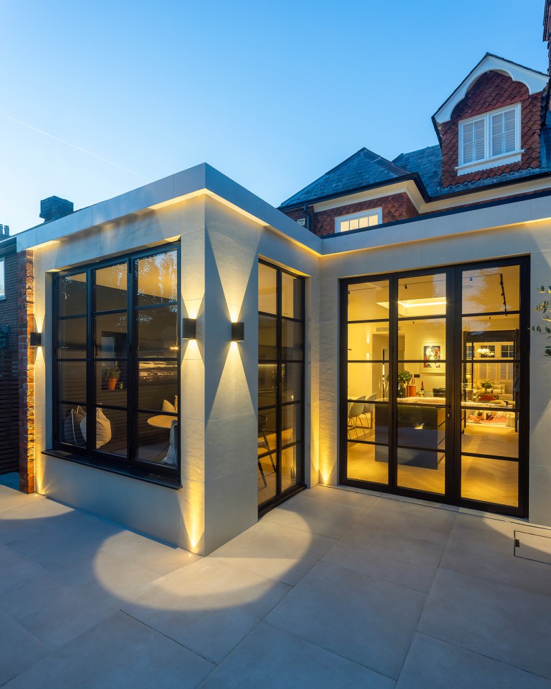 Evening view of modern home extension with black-framed glazing, stone cladding, and architectural LED lighting